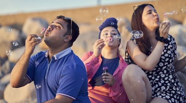Three students blowing soap bubbles outside. Photograph.