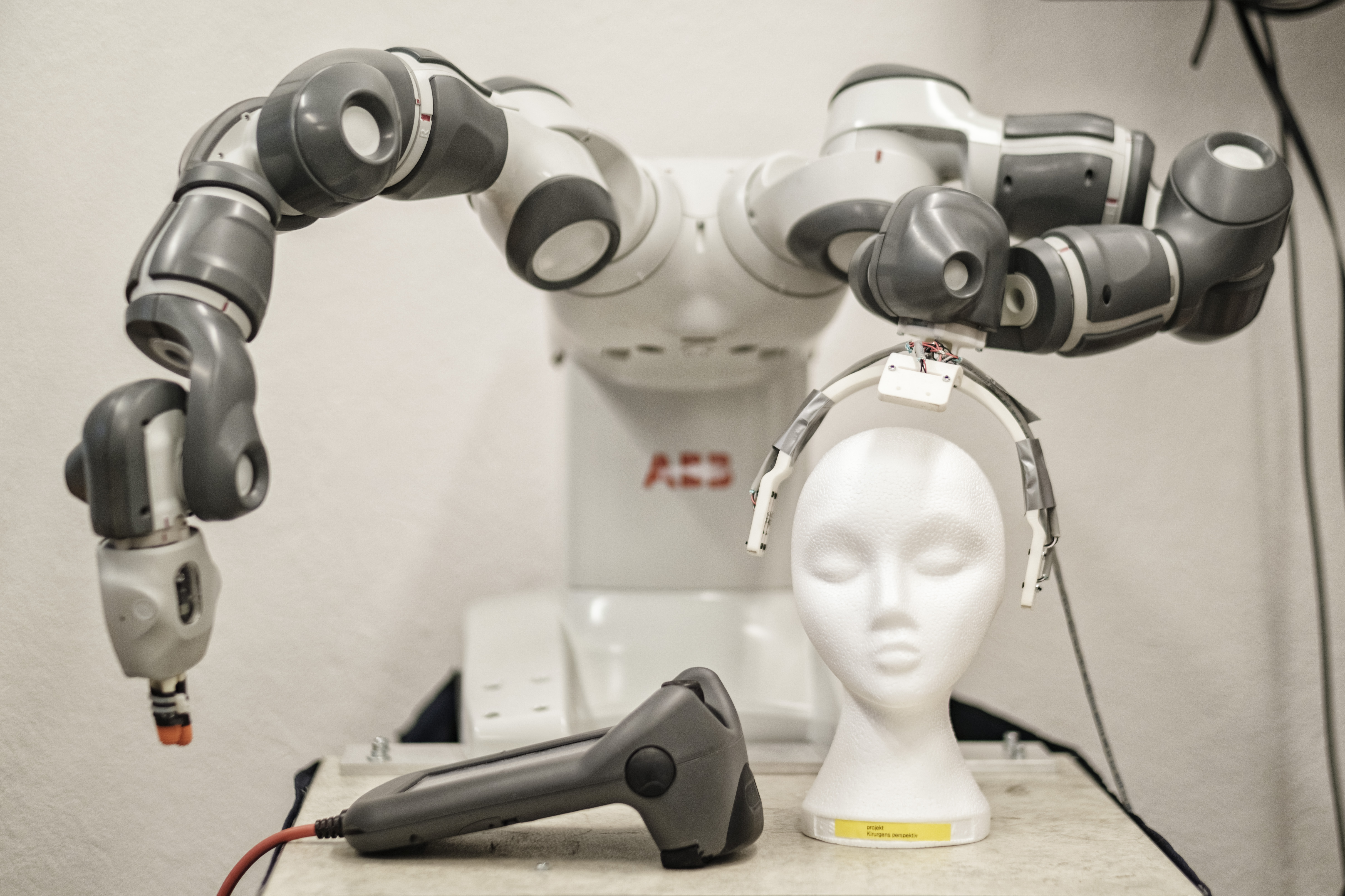 Två robotarmar bakom ett människoliknande huvud av frigolit, i Robotlabbet på LTH.