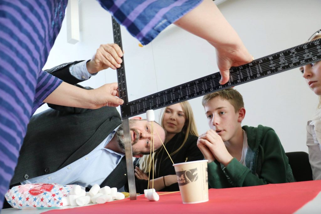 Elever tittar på en lärare som håller en linjal vilken är del av ett experiment.