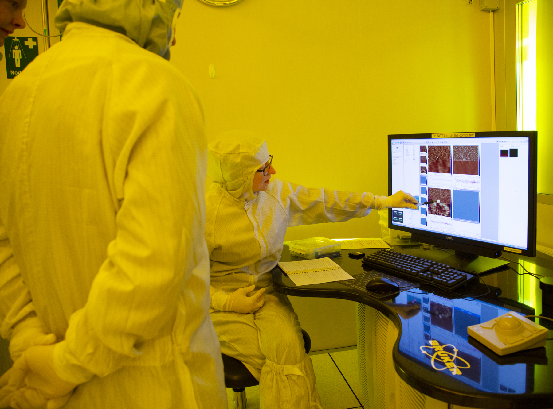 Researchers in protective clothing looking at a computer screen. Photo.