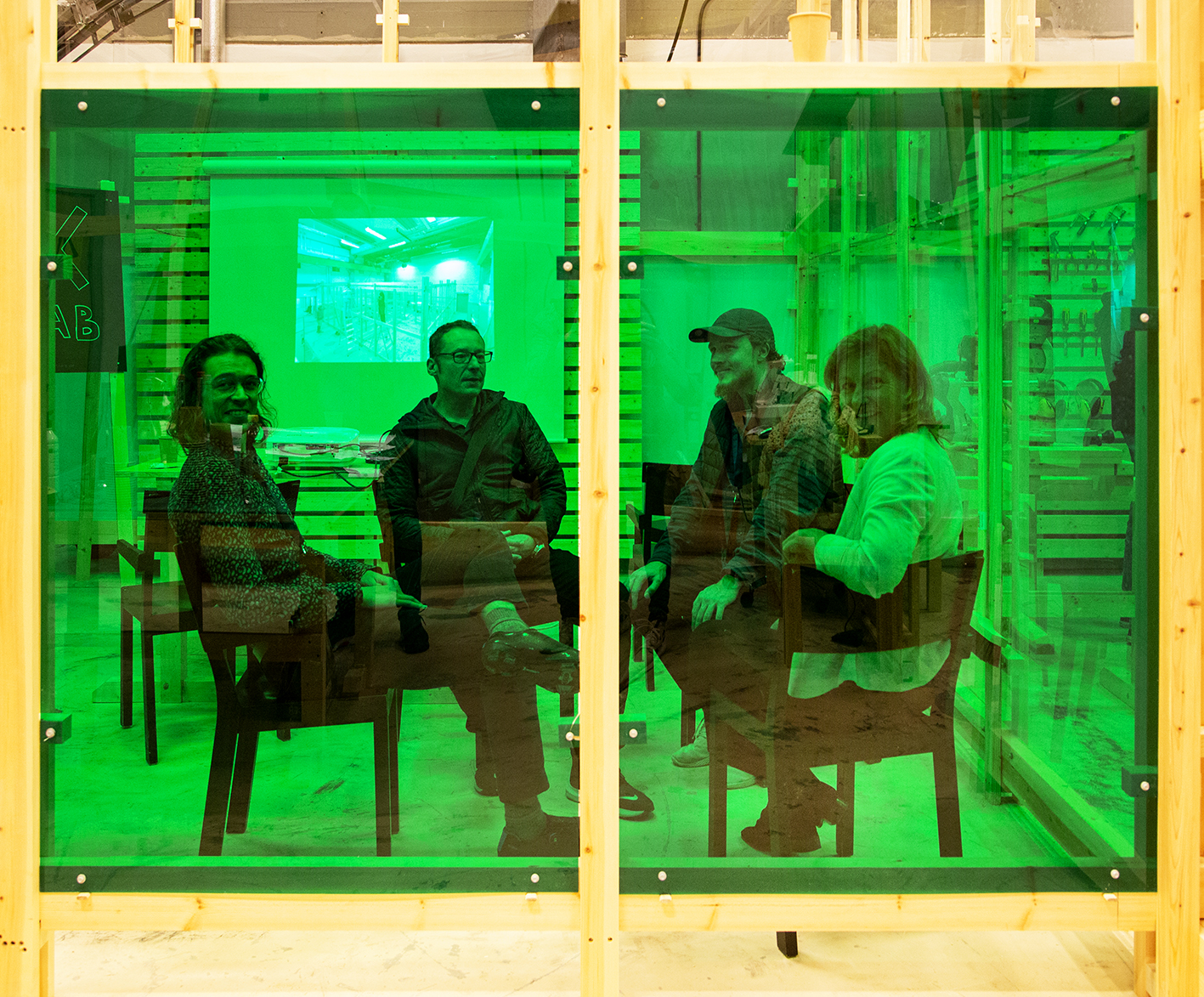 A group of people smiling and talking behind a green glass wall. Photo. 