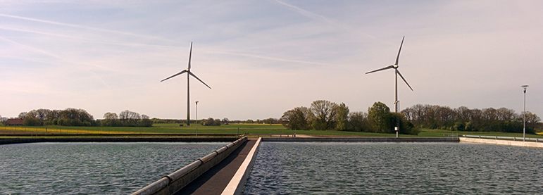 A photo of water, a bridge and two wind turbines.
