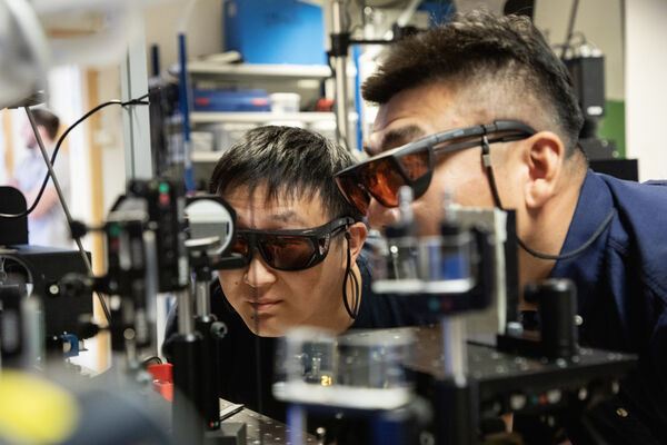 Två forskare med skyddsglasögon tittar på forskningsutrustning.