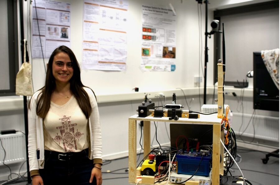 Photo. A person standing beside a table with electronic equipment.