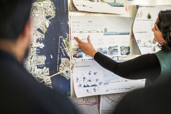 En person pekar på och berättar om ritningar som är upphängda på en vägg.