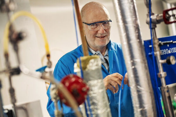 En forskare med skyddsglasögon står bakom en forskningsanläggning.