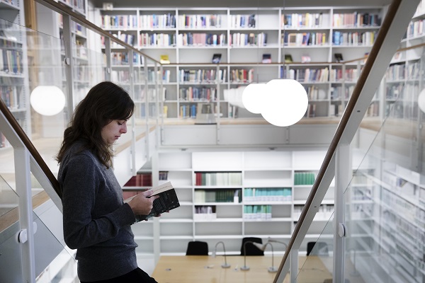 Person läser en bok i ett bibliotek. Foto.