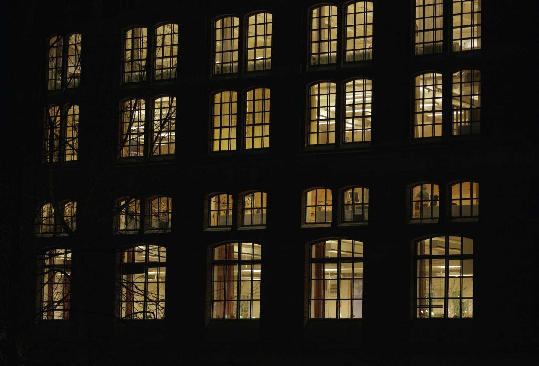 Fönster i äldre byggnad. Natt eller kväll, lamporna lyser gult i fönstren. Foto.