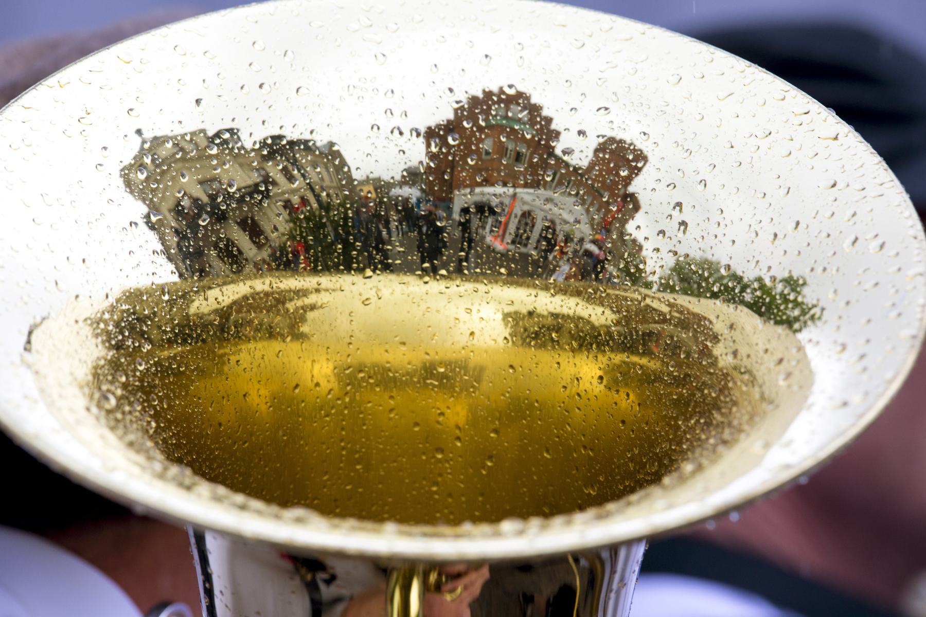 Lund University main building and AF-borgen are reflected in a brass instrument, probably a tuba, with raindrops in it.