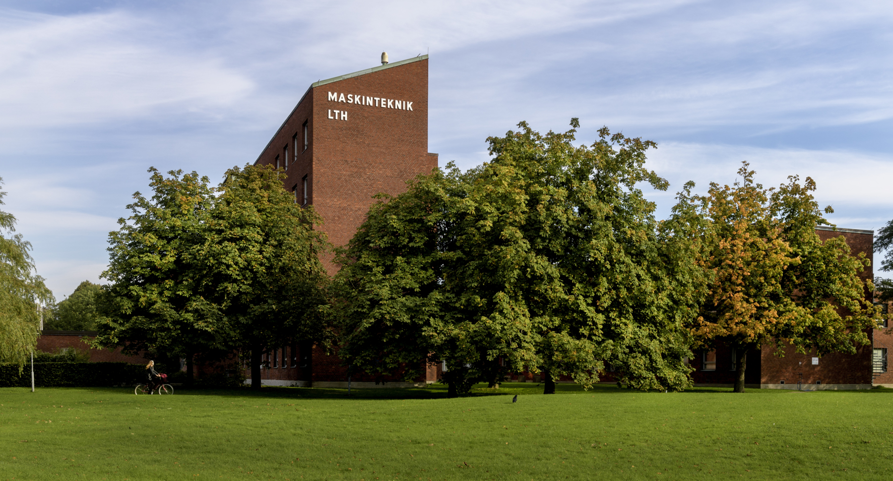 M-huset på LTH:s campus, inbäddat i gröngula trädkronor och med stor gräsmatta framför.