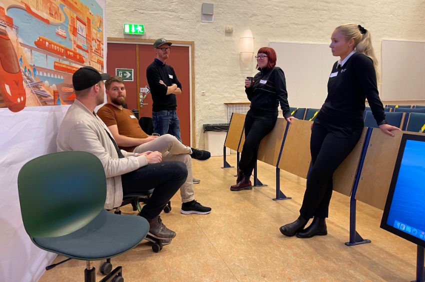 En handfull tidigare studenter talar i en föreläsningssal på Campus Helsingborg, i bakgrunden syns en tecknad affisch om framtidens trafik. Foto.