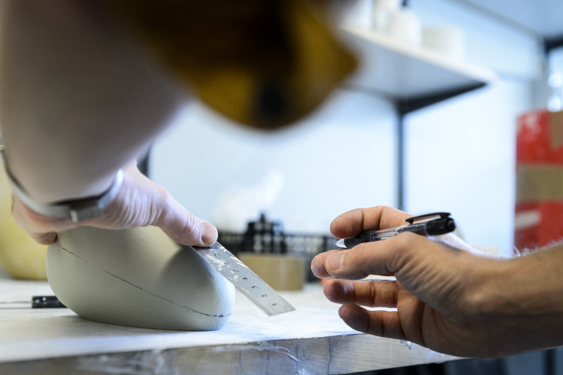 A pair of hands working on a desk with what appears to be a bit of gray plastic. Photo.