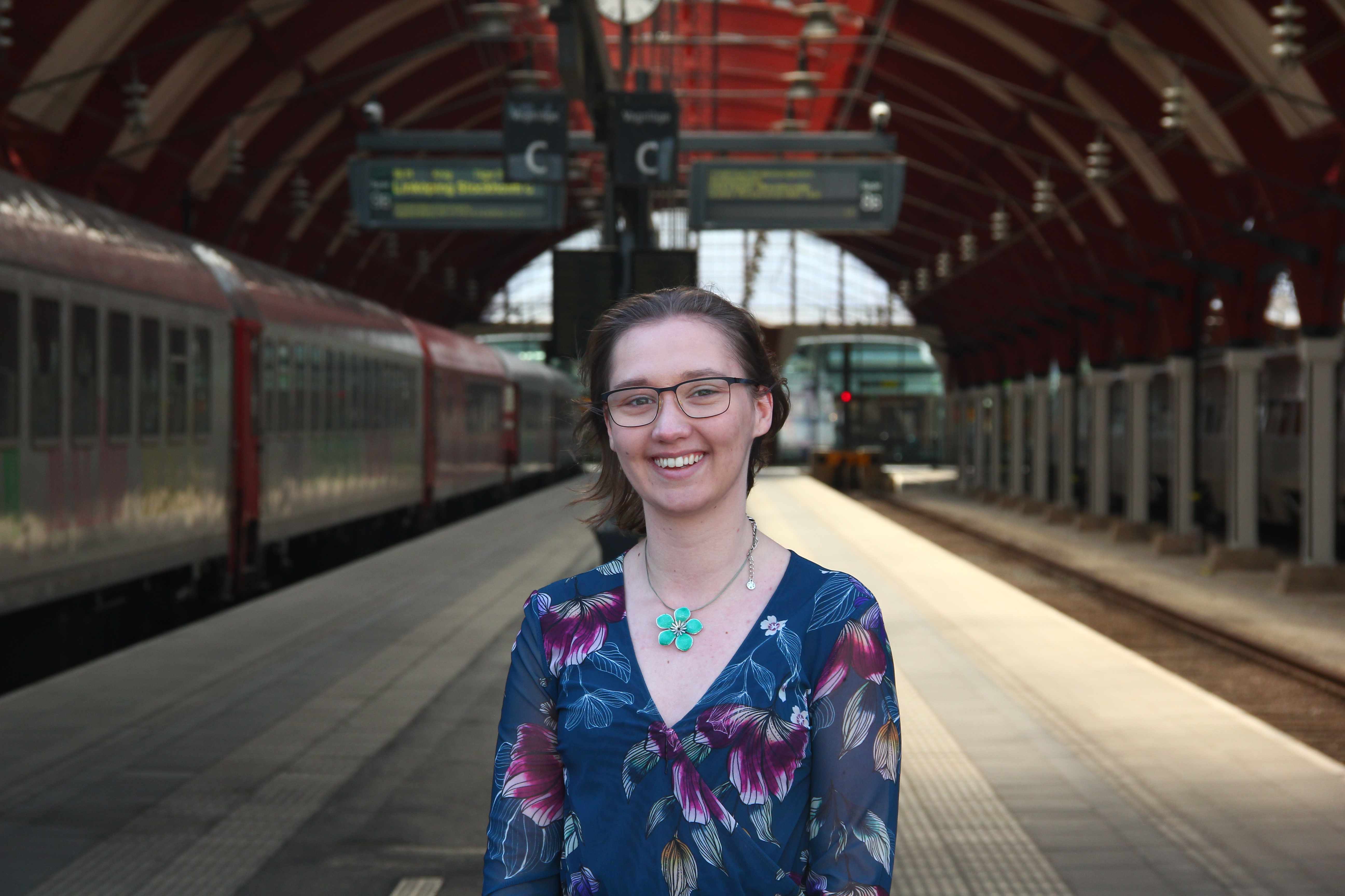 Porträttfoto av Emma Dyrssen med tågstation som bakgrund. Foto.