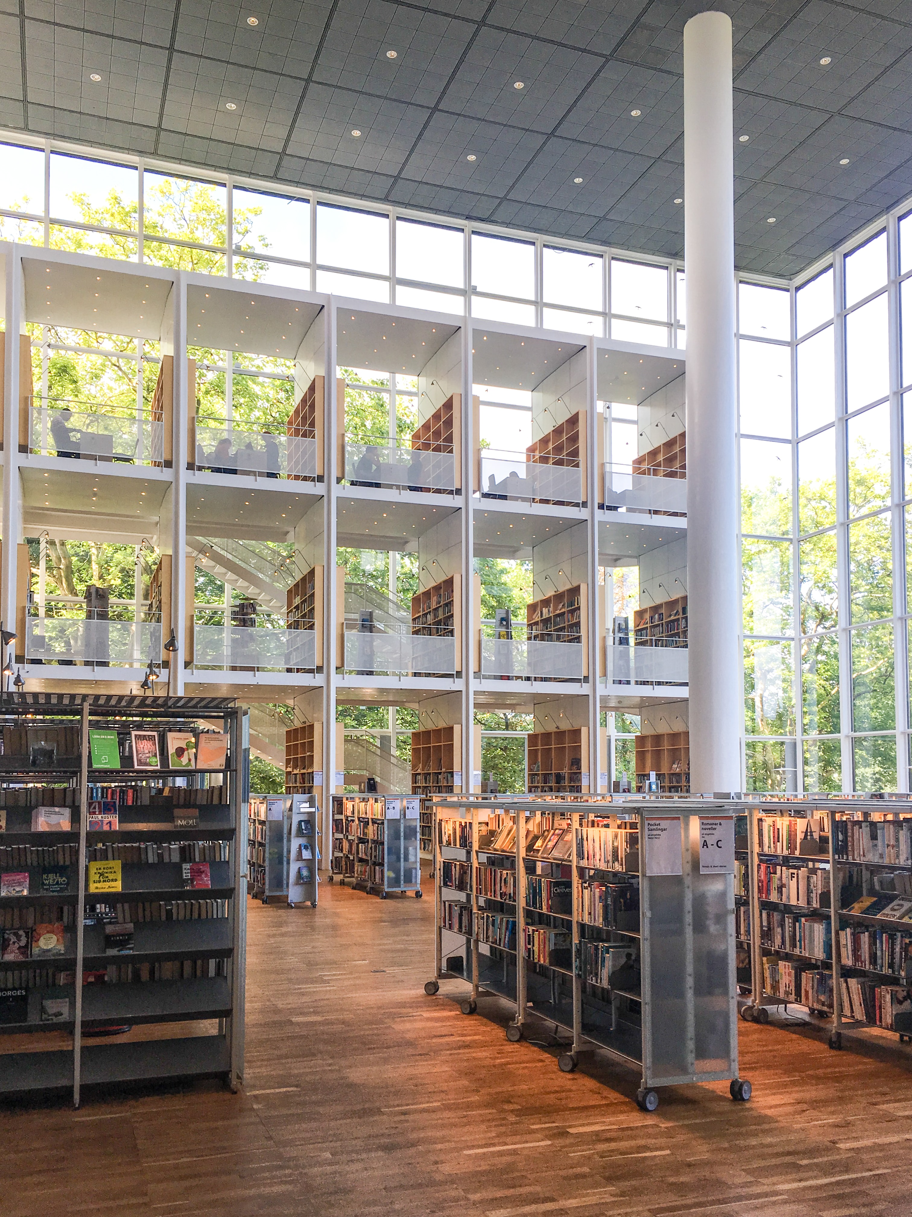 Vy från Malmö stadsbibliotek, bokhyllor framför stora fönster, mycket högt i tak. Foto.