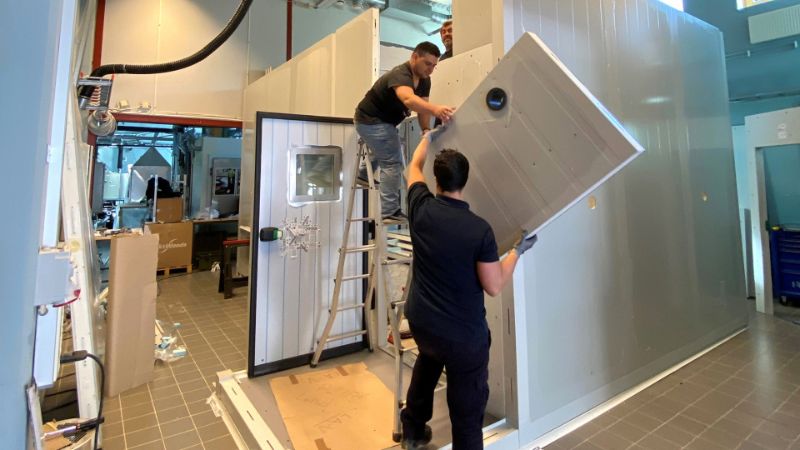 Two people lift a piece of wall into place in a half-finished room.