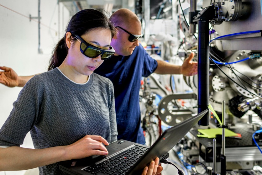 Två personer med stora solglasögon jobbar inne på Max IV, den ena tittar på en bärbar dator som hon har i handen.
