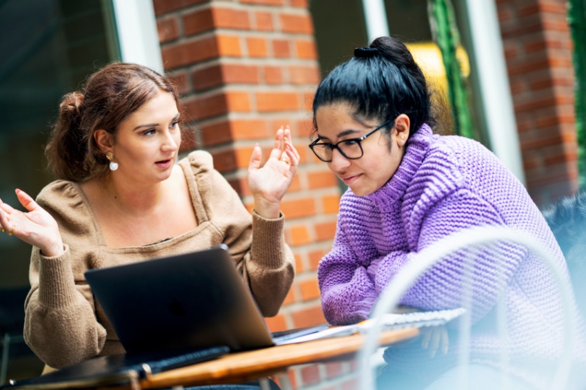 Two female students discuss in front of a computer.