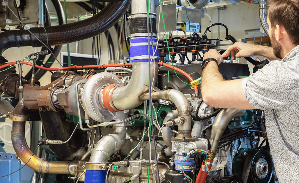 An engine part is seen while a man in profile works on the technology. Photo.