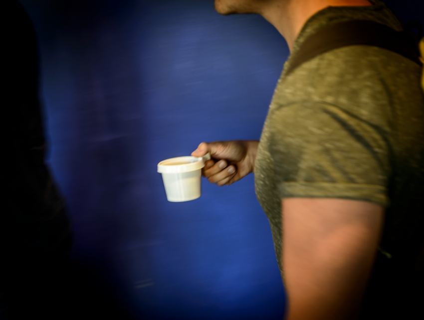 Student bär på en vit kaffekopp, i bakgrunden en blå vägg.