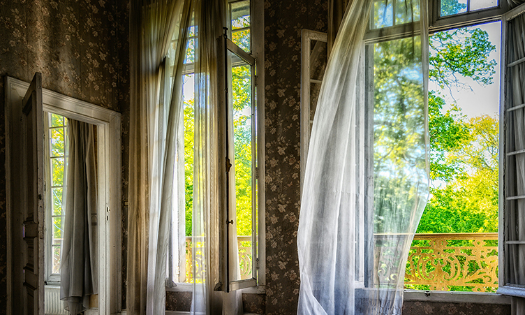 Fönster som är öppna med fladdrande gardiner. Foto.