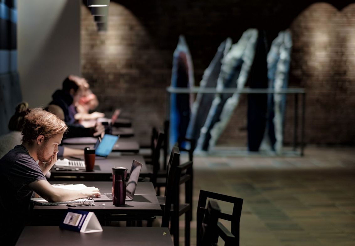 Studying students behind tables with art work in the background. Photo.