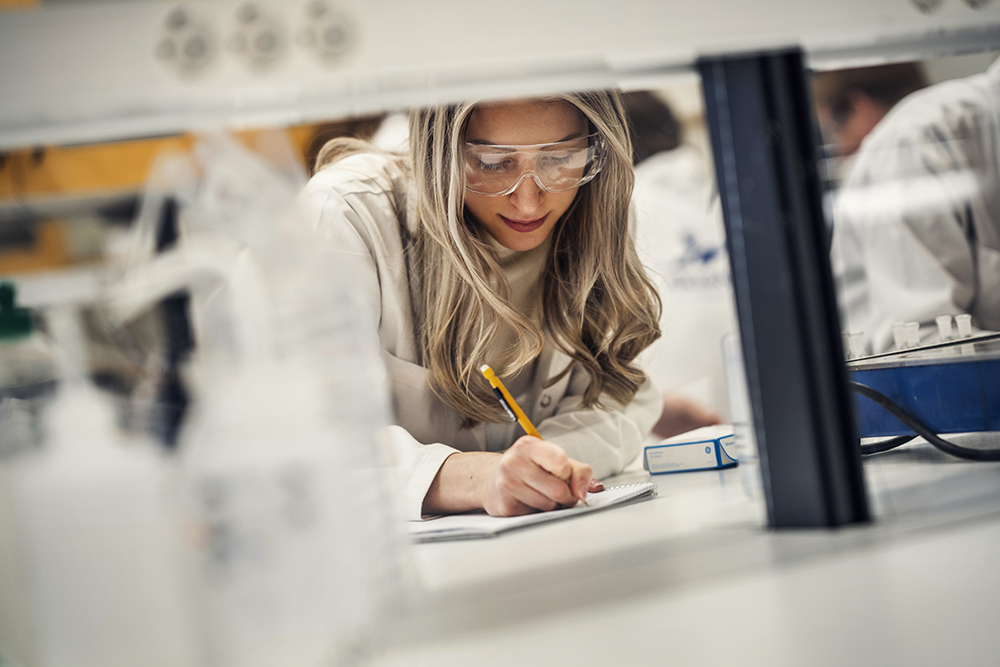 Student in lab writing on a noteblock. Photo.