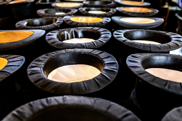 Black doctoral hats lined up, upside down. Inside it looks as if there is white or yellow silk. Photo.